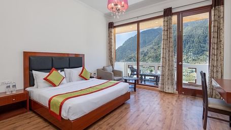 The image shows a hotel room with a large bed, a sitting area with a sofa and coffee table, and a large window with a view  | DLS Serenity Resort and Spa